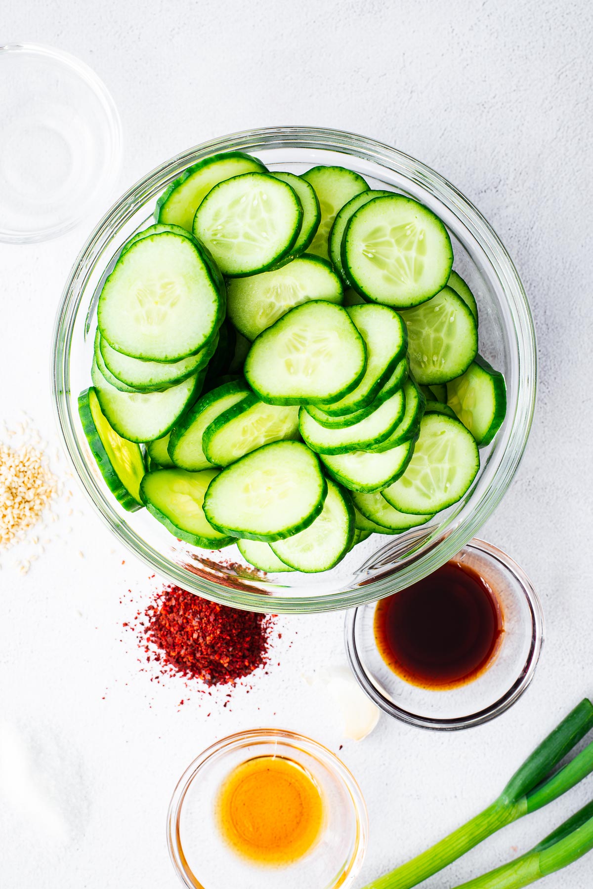 Korean cucumber salad ingredients, including sliced cucumber, spring onions, soy sauce, gochugaru flakes, sesame seeds, toasted sesame oil, rice vinegar and sugar.