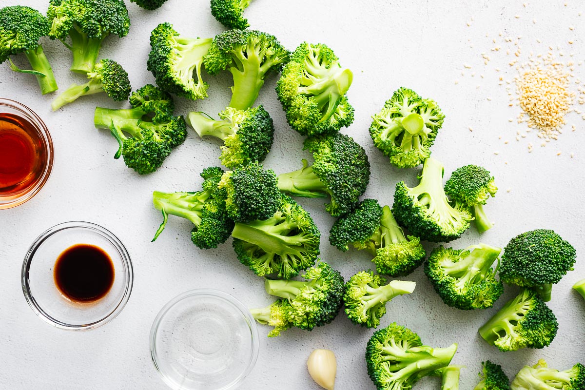 Asian sesame broccoli salad ingredients, including fresh broccoli florets, sesame seeds, garlic, rice vinegar, soy sauce and sesame oil.
