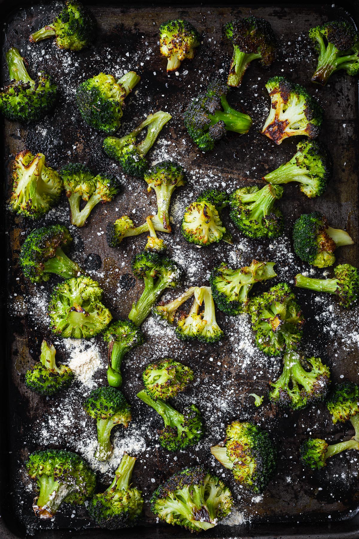 Oven-roasted frozen broccoli sprinkled with garlic salt on a baking sheet viewed from above.