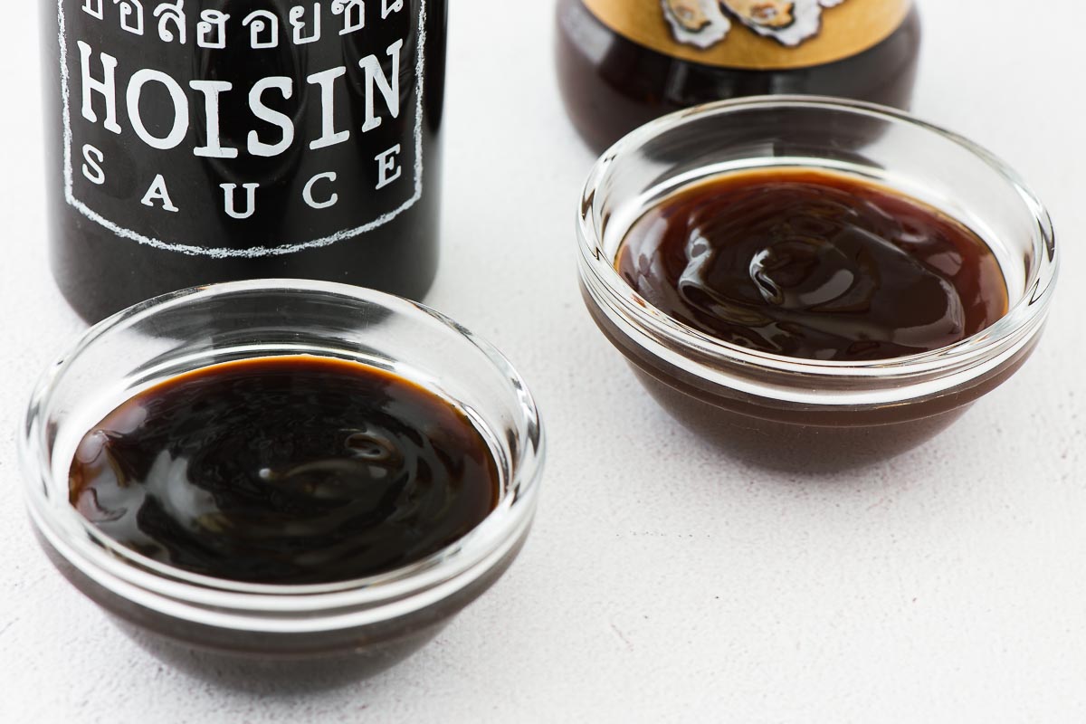 Hoisin sauce and oyster sauce in glass bowls with sauce bottles behind them.