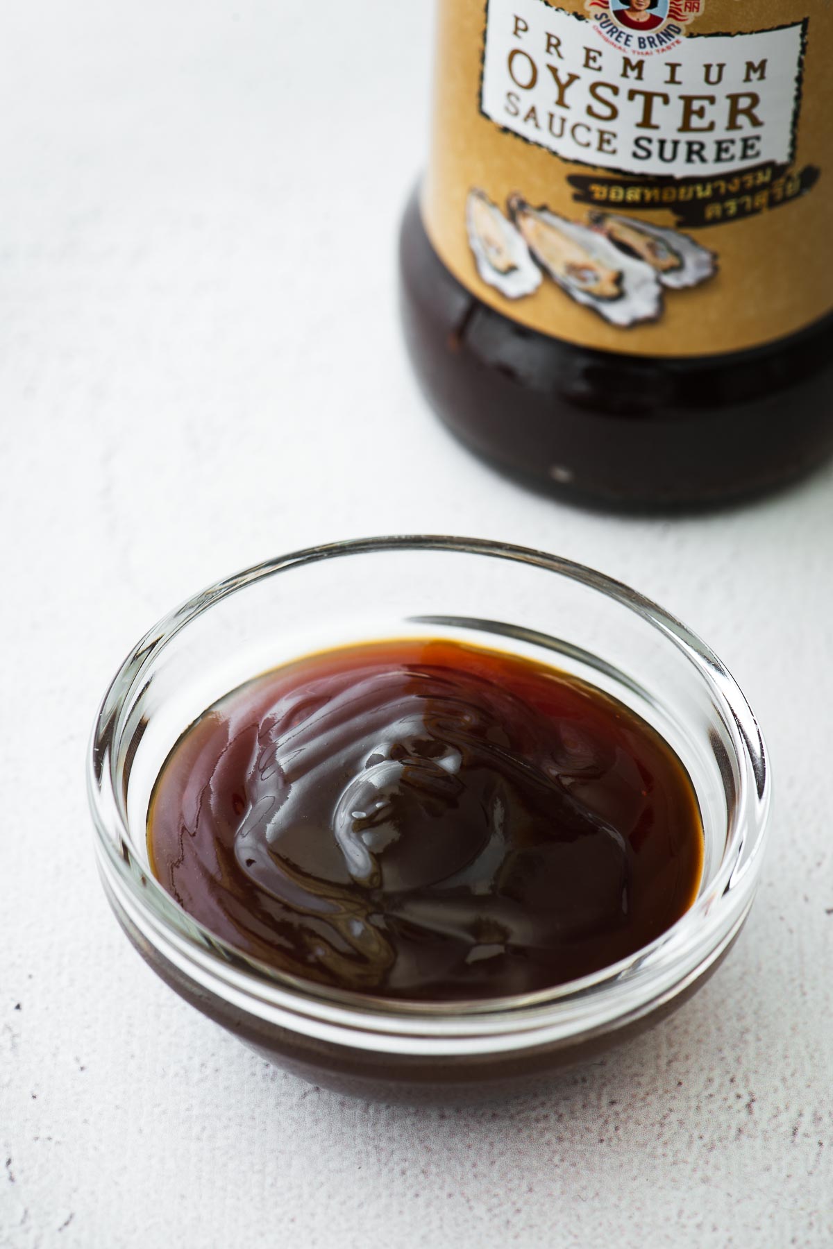 Oyster sauce in a small glass bowl with an oyster sauce bottle in the background.