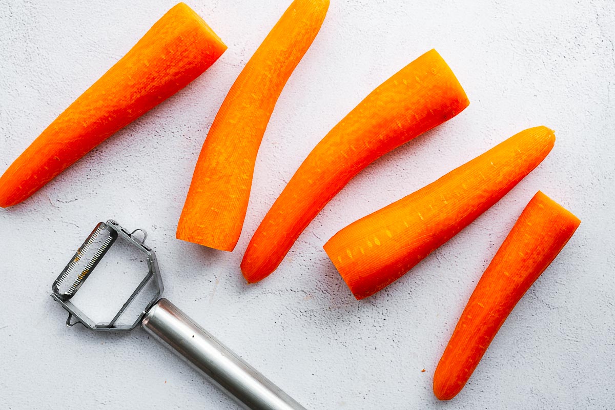 Peeled whole carrots with a vegetable peeler on a concrete background.
