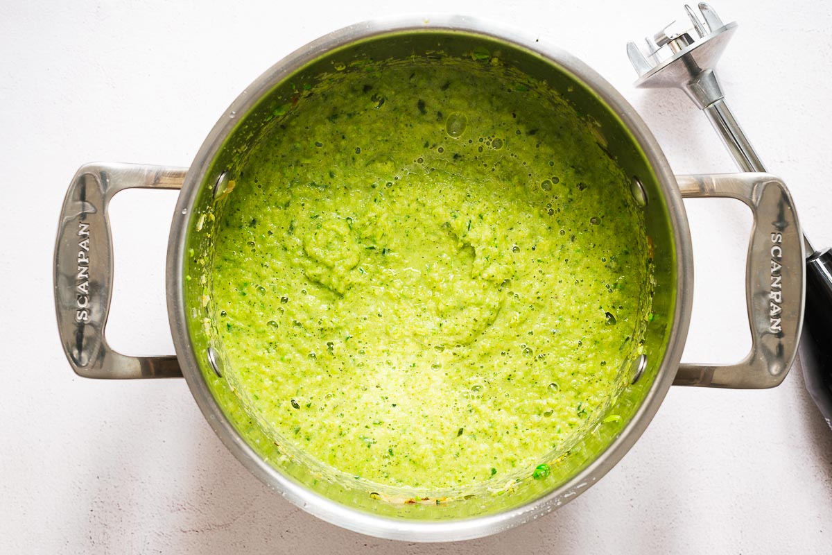 Spring green broccoli and pea soup in a stainless steel pot with an immersion blender.