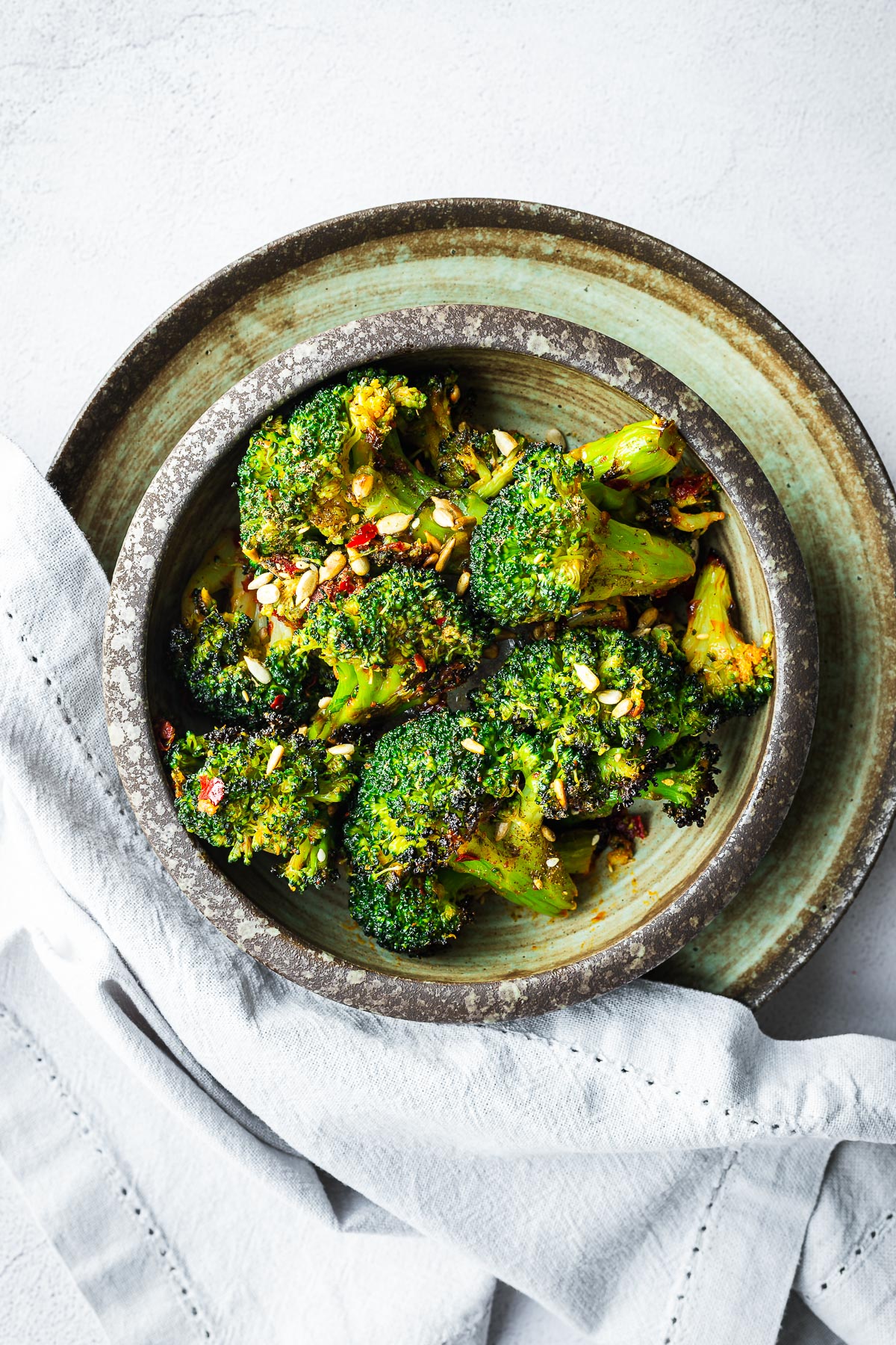 Oven-roasted frozen broccoli with harissa oil and sunflower seeds in a brown ceramic bowl.