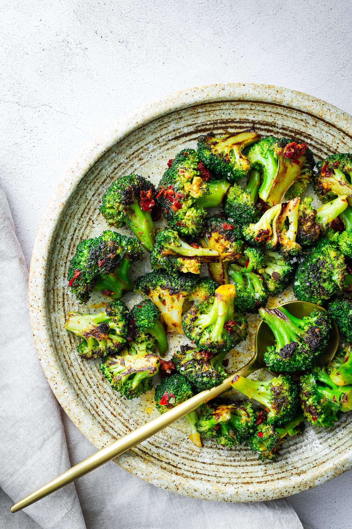 Sautéed frozen broccoli with harissa in a ceramic bowl with a gold serving spoon.