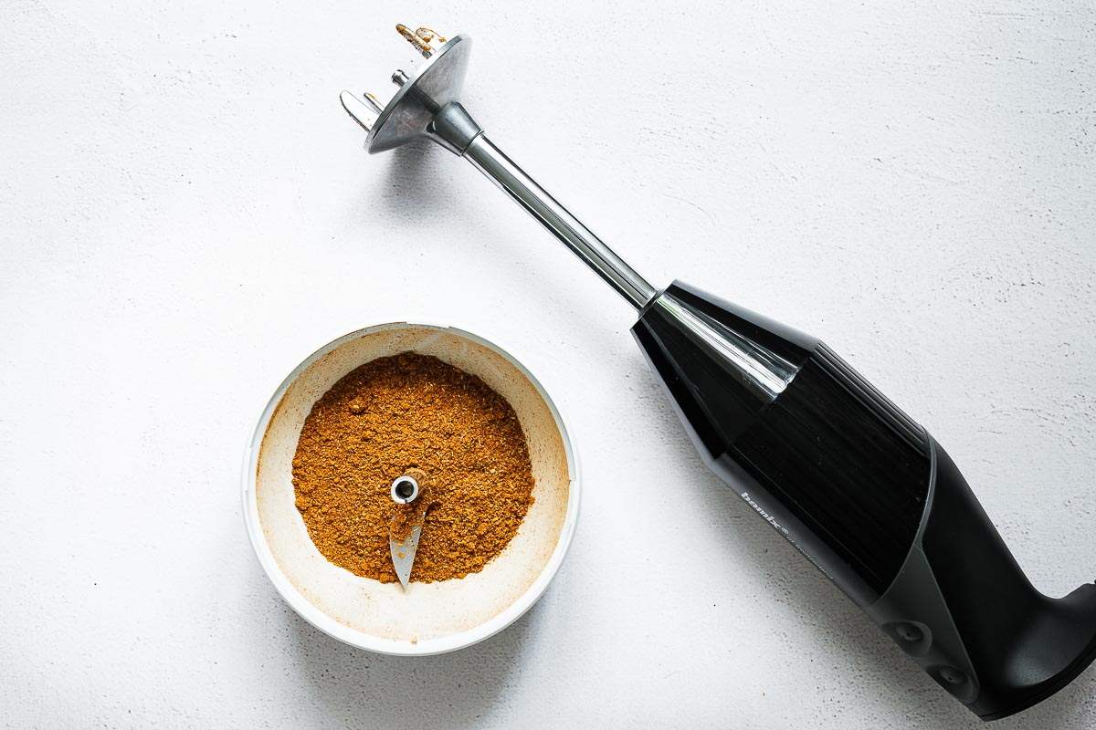 Chinese five-spice powder in a small food processor attachment next to an immersion blender viewed from above.