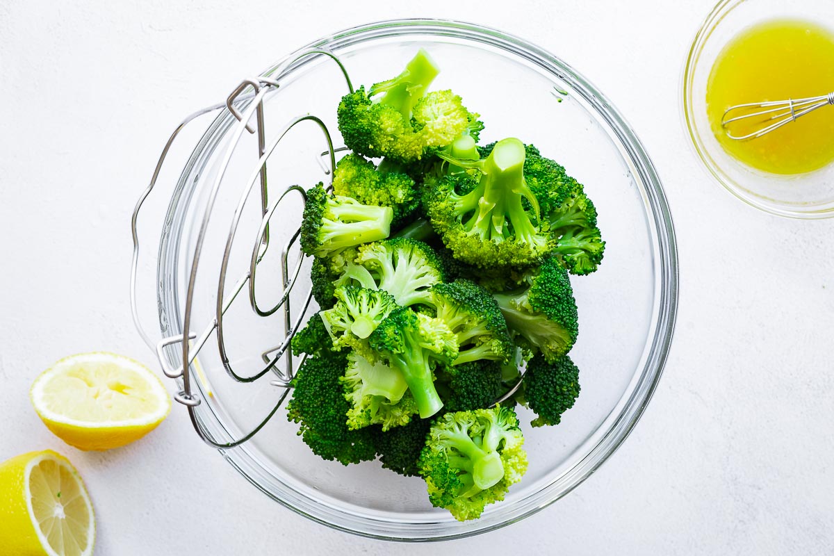 Tipping Instant Pot broccoli from the steamer trivet with handles into a glass mixing bowl.