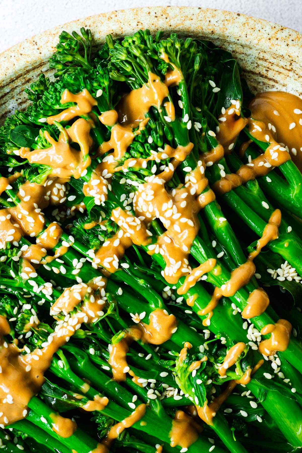 A close-up of steamed broccoli drizzled with Japanese sesame sauce and sesame seeds.