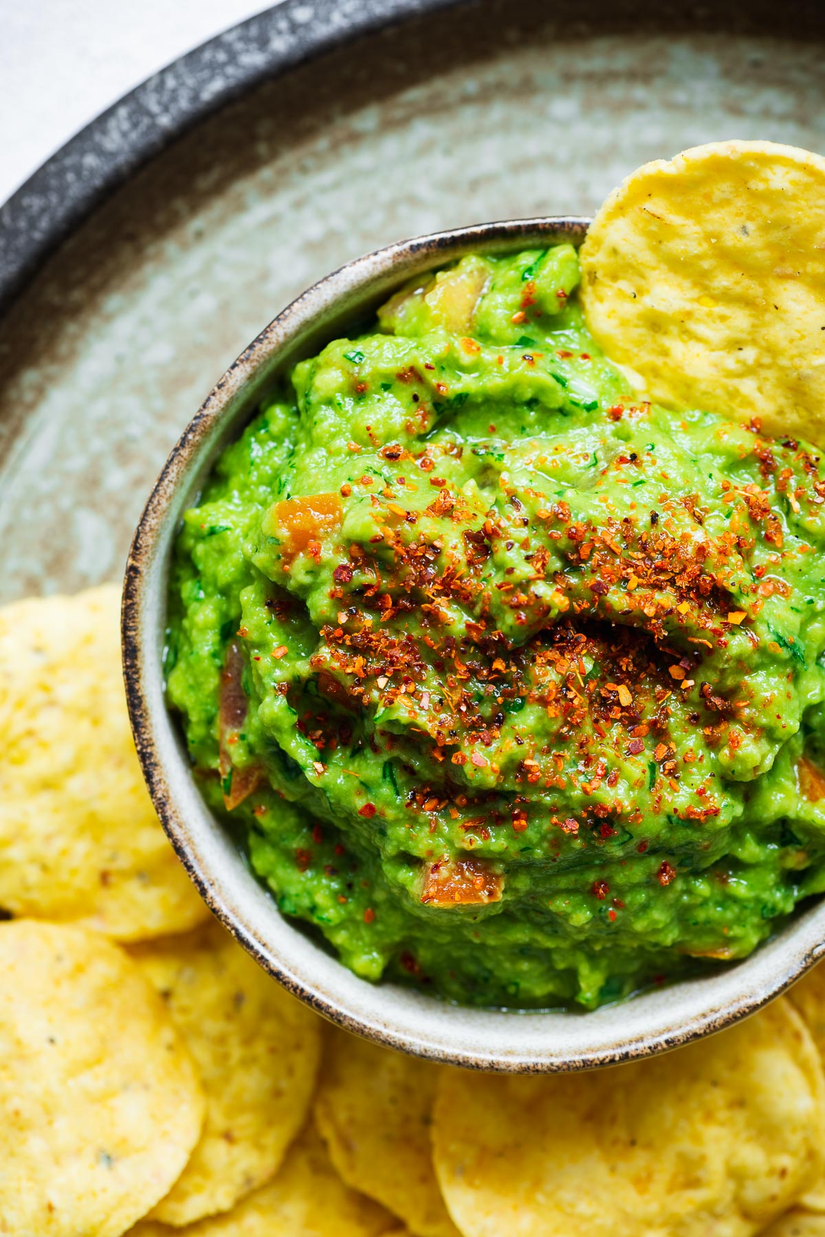 Defrosted guacamole loaded with tomatoes, green onions, cilantro and topped with tajin seasoning in a small bowl viewed from above.