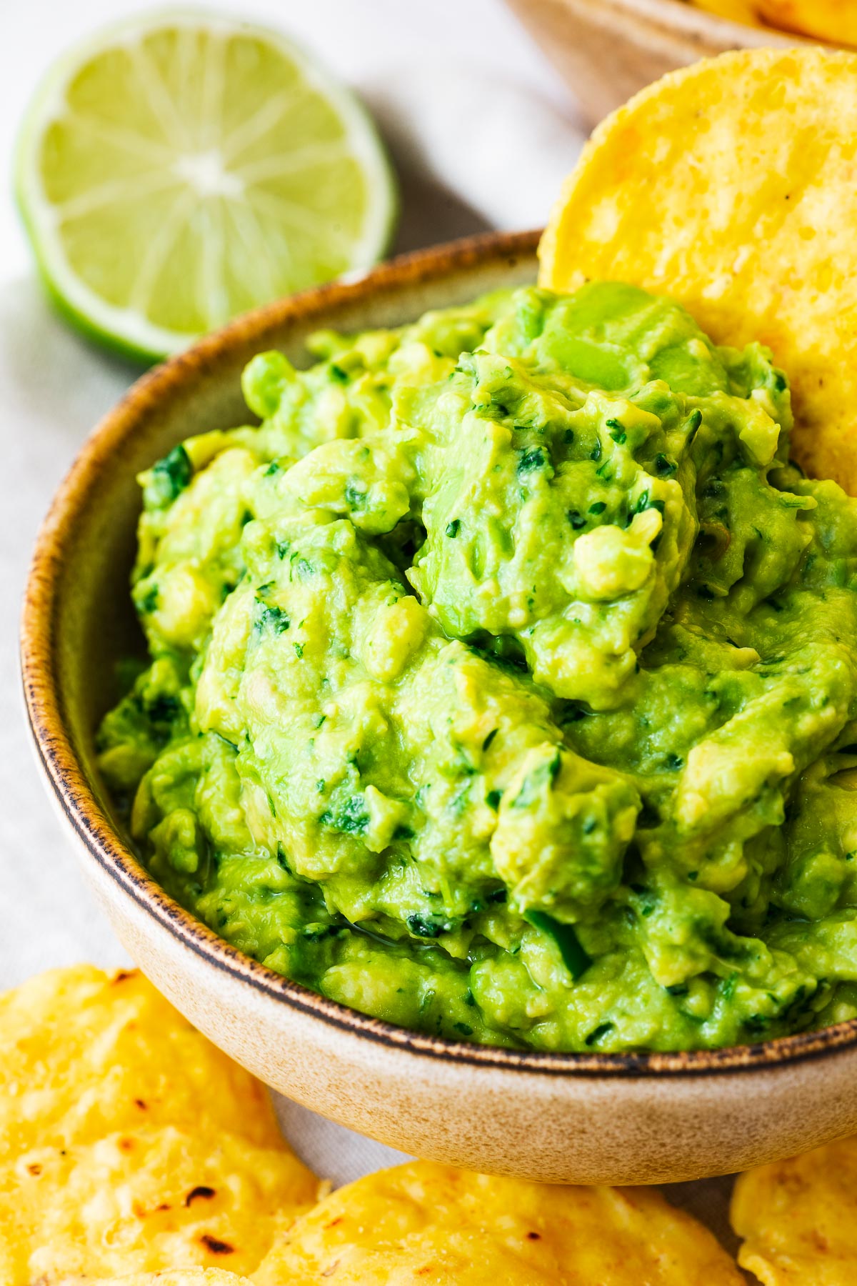Close-up of a bowl of creamy guacamole without onions with a tortilla chip and sliced lime in the background.