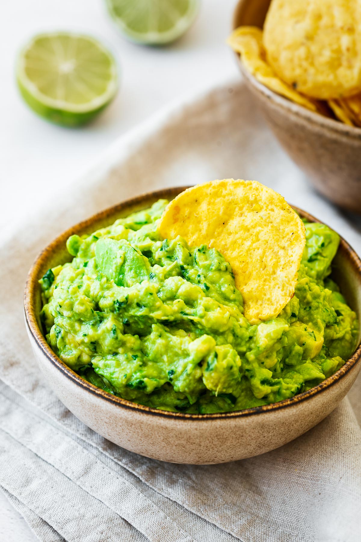 Chunky guacamole without onions or tomatoes with a corn chip and sliced lime in the background.