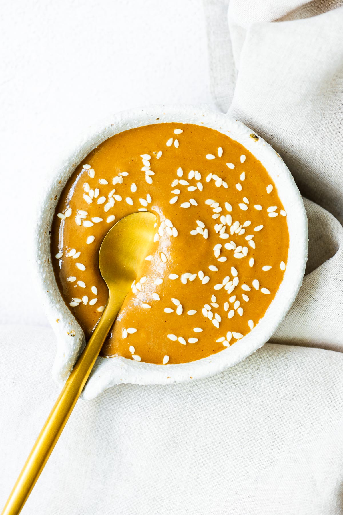 Close-up of Japanese sesame sauce (goma dare) sprinkled with sesame seeds, served with a gold spoon.