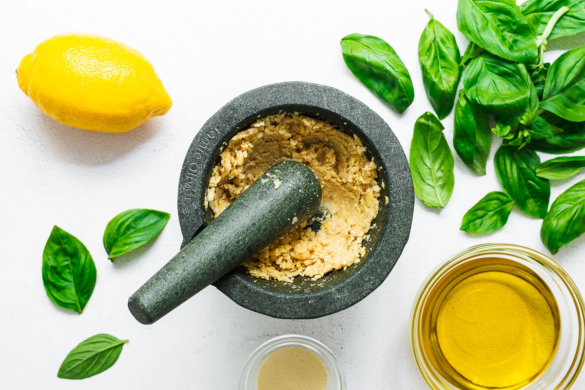 Garlic and pine nuts pounded into a creamy paste in a mortar and pestle for making basil pesto.