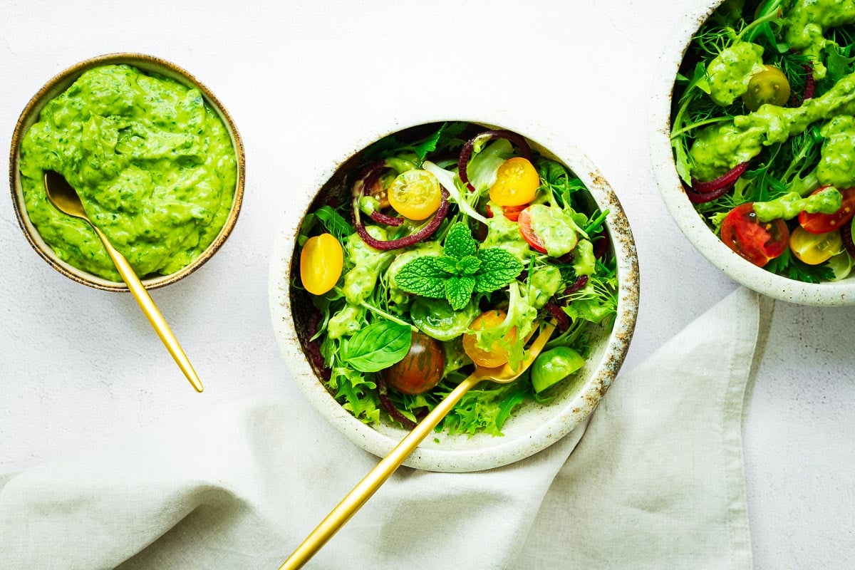 A top down view of salad bowls with an avocado green goddess salad dressing.