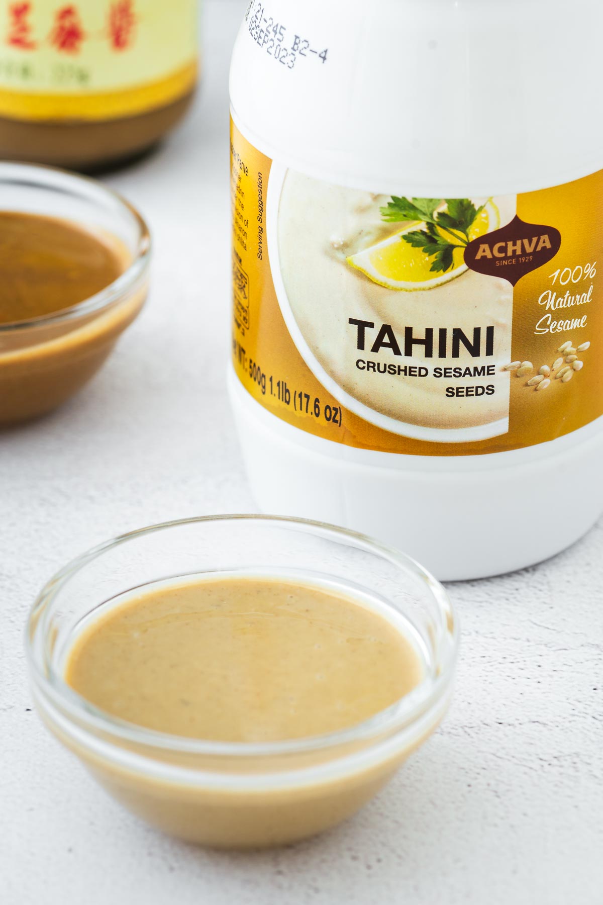 Light coloured tahini paste in a small glass bowl with darker sesame paste in the background.