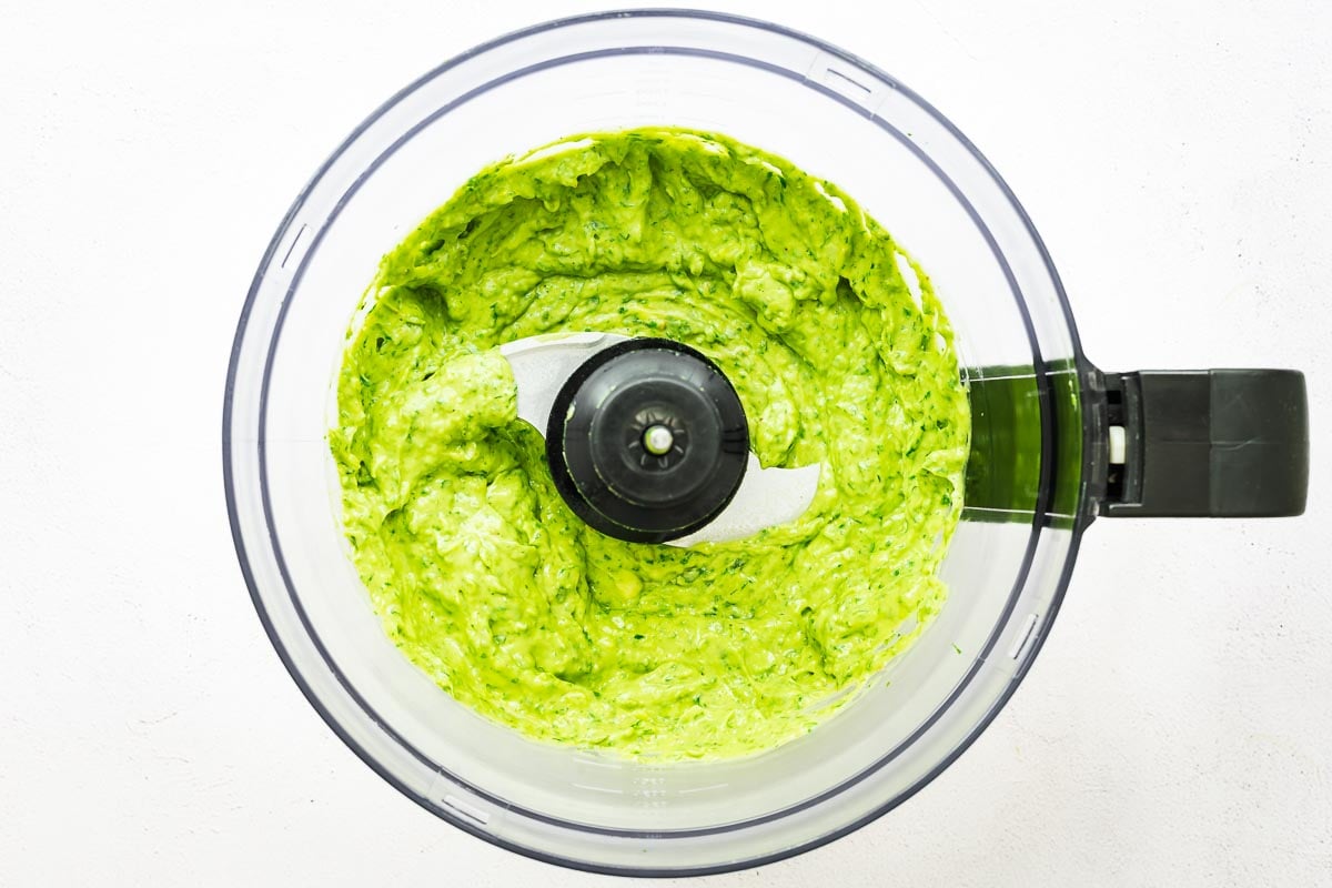 Smooth and creamy vegan green goddess sauce in a food processor bowl.