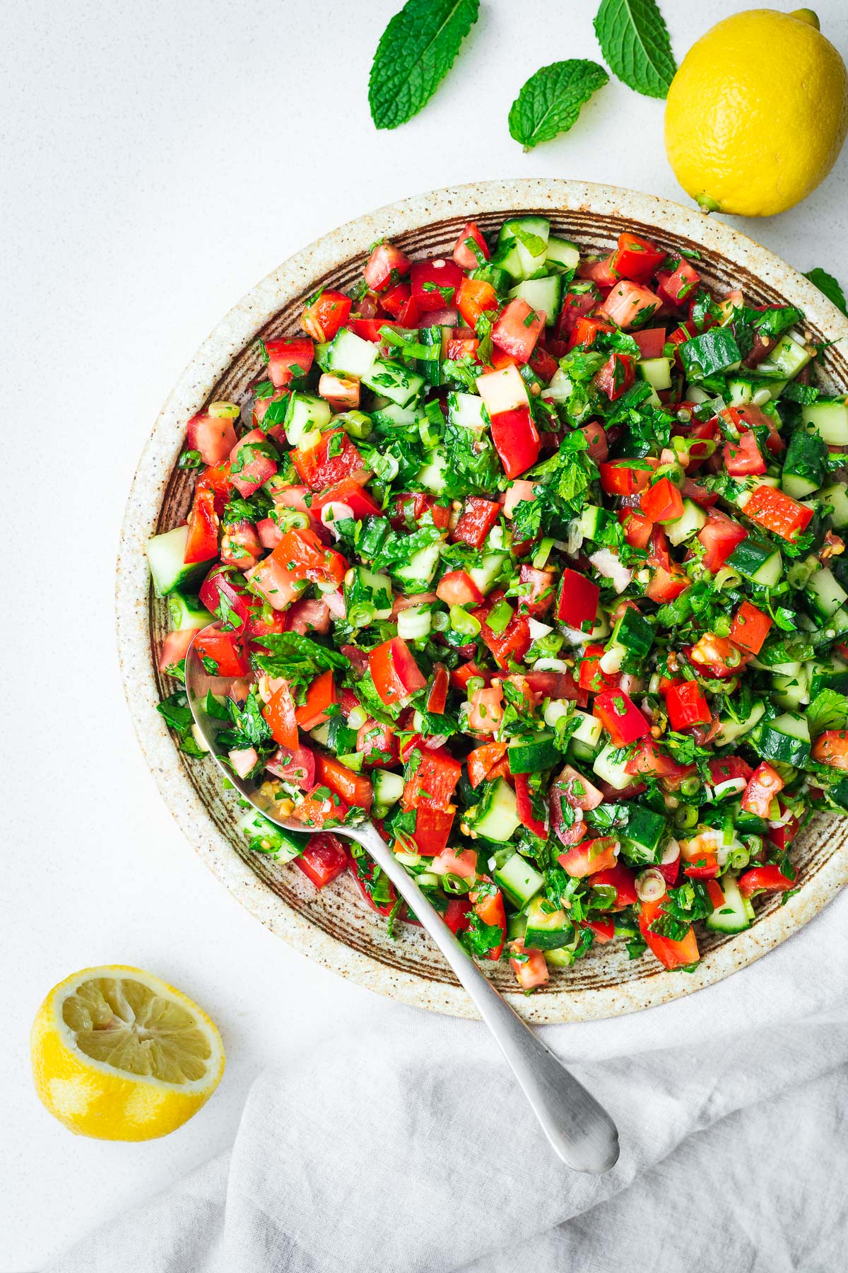 A fresh Arabic chopped salad on a serving plate with a silver spoon, viewed from above.