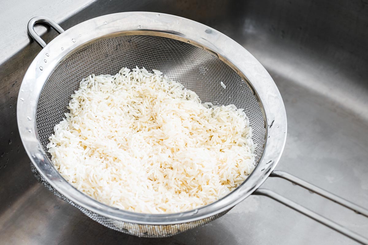 Long-grain rice draining in a mesh strainer over the kitchen sink.