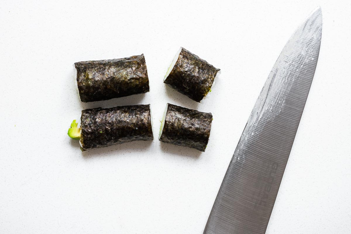 A sharp knife with a sushi maki roll being cut.