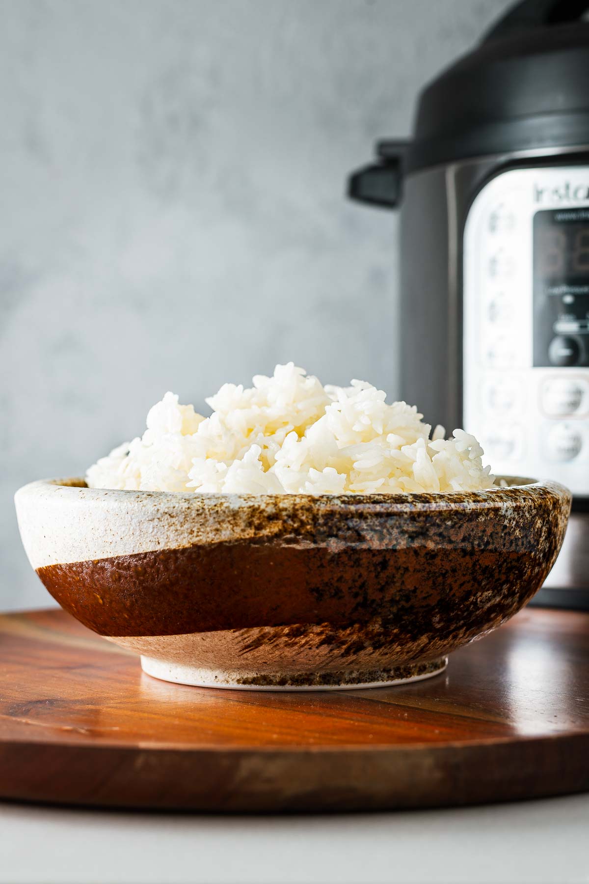 A ceramic bowl with fluffy Jasmine rice (long-grain rice) in front of an Instant Pot pressure cooker.