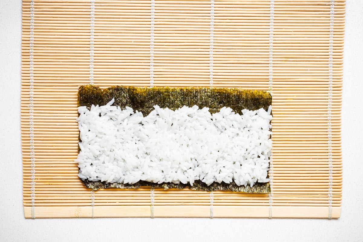 Top down view of nori seaweed with a thin layer of rice on a bamboo mat.