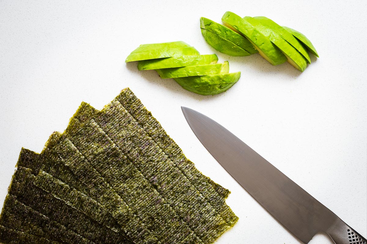 Slices of avocado and nori sheets with a sharp knife.