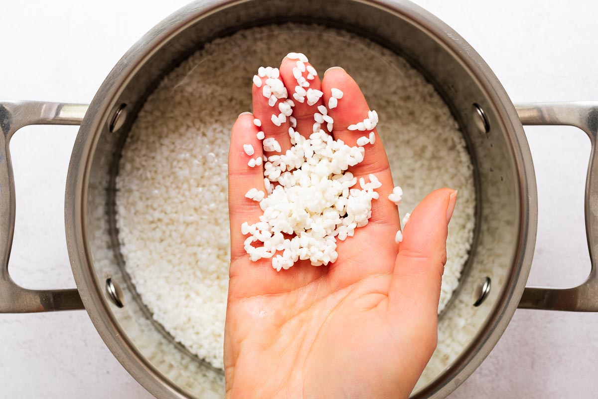 A hand holding soaked white rice. The rice is opaque after soaking.