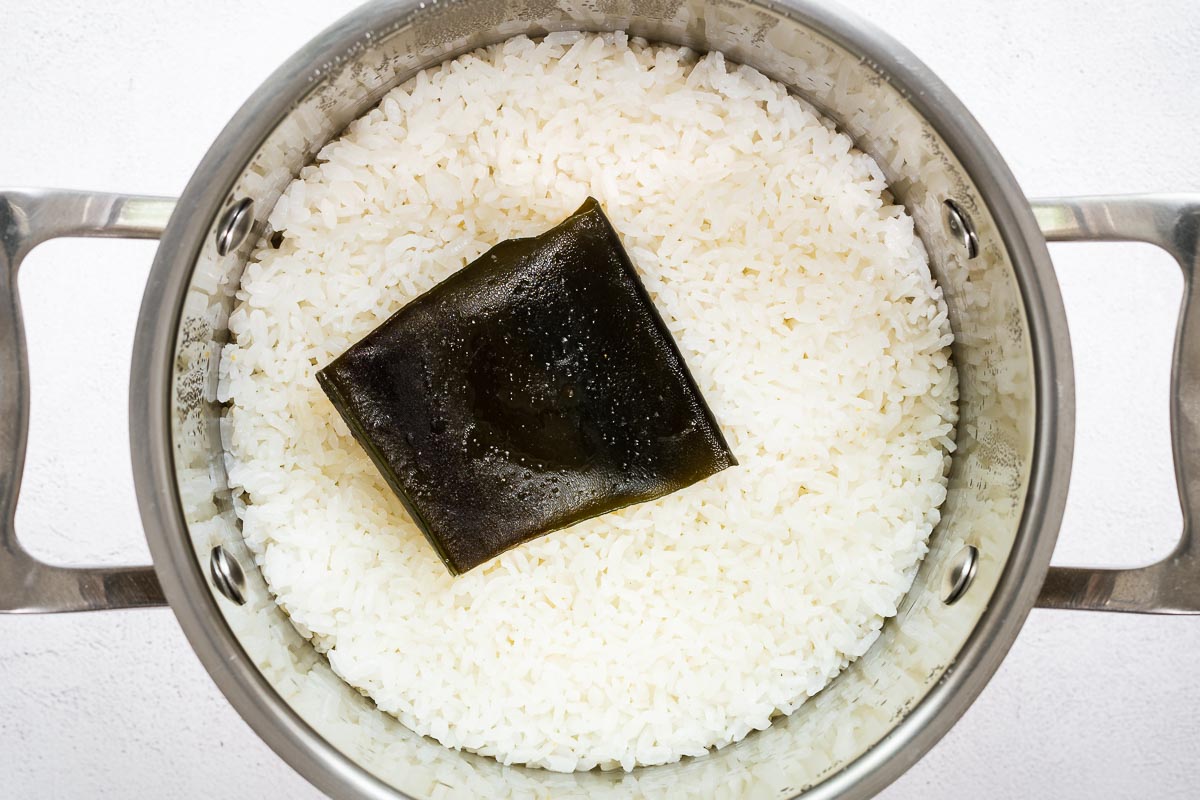 Stovetop cooked sushi rice with a piece of rehydrated kombu in a pot, viewed from above.