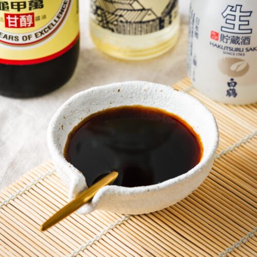 A bowl of sukiyaki sauce surrounded by ingredients, including Kikkoman soy sauce, mirin and sake.