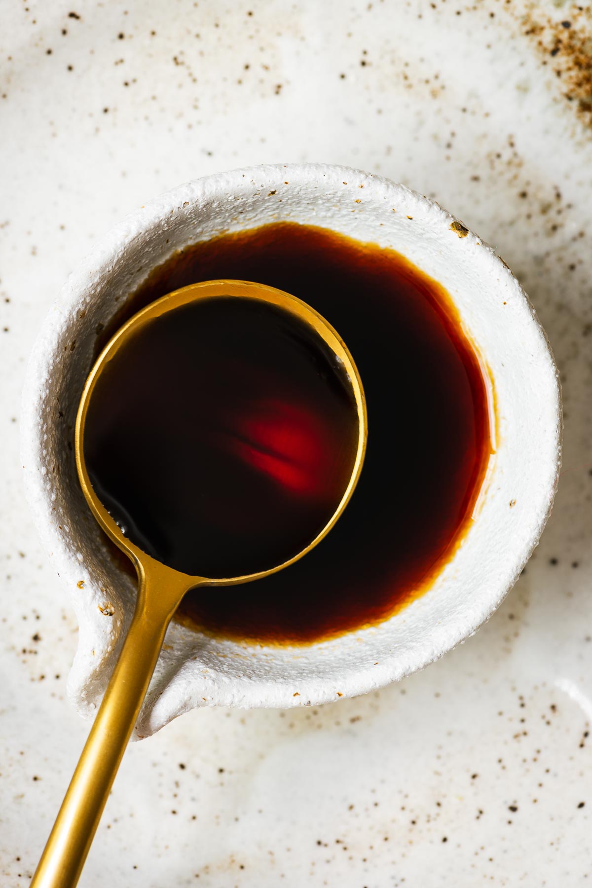 A close-up of sukiyaki sauce in a small soy sauce bowl with a gold tablespoon.