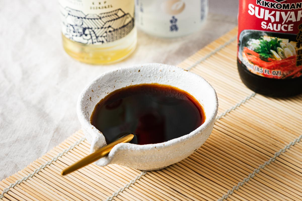 Sukiyaki sauce in a sauce bowl with a bottle of Kikkoman sukiyaki sauce in the background.