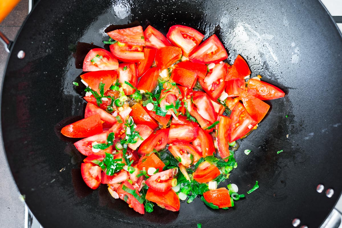 Tomatoes, spring onions and garlic in a wok.