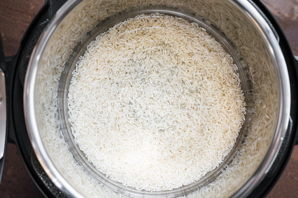 Top down view of uncooked jasmine rice in the Instant Pot inner pot with water and salt.