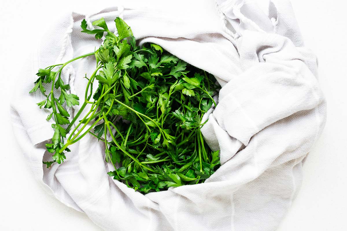 Washed parsley being dried in a light grey kitchen towel viewed from above.