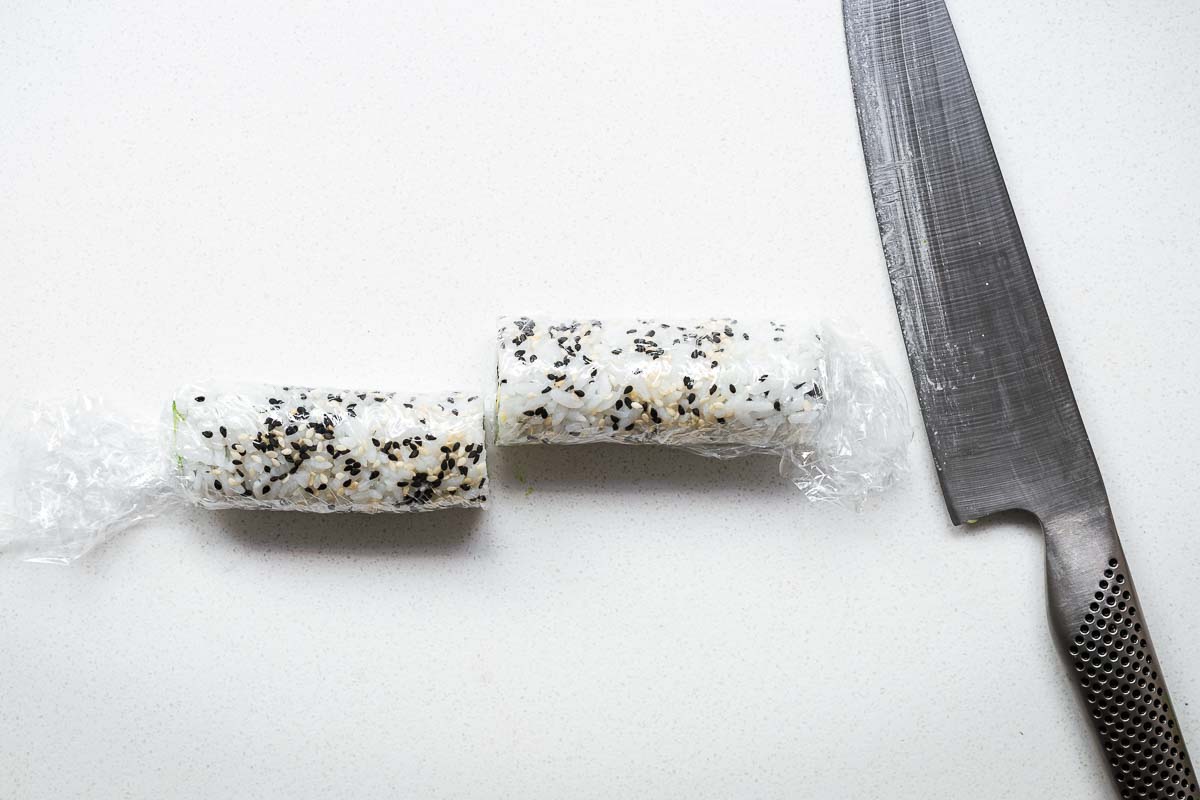 An inside-out sushi roll wrapped in cling wrap and sliced in half with a sharp knife.
