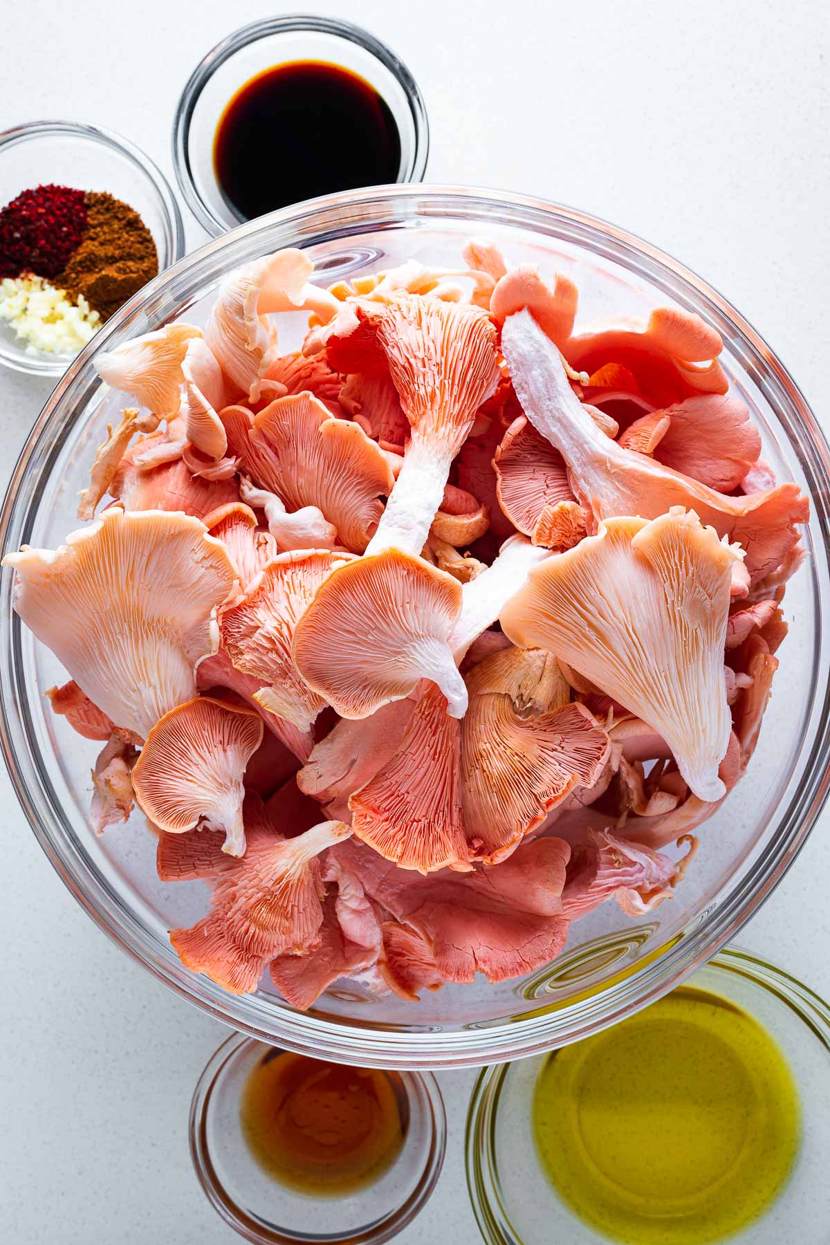 Top down view of a bowl of pink oyster mushrooms surrounded by multiple small bowls with marinade ingredients.