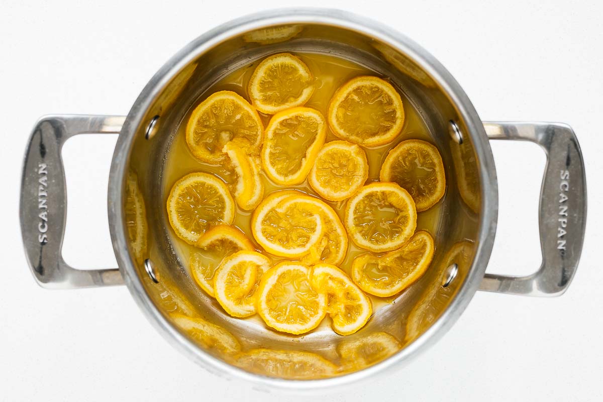 Slices of fresh lemon cooked in lemon juice and salt for 14 minutes in a saucepan, viewed from above.