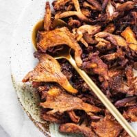 A close-up of roasted pink oyster mushrooms with a golden serving spoon.