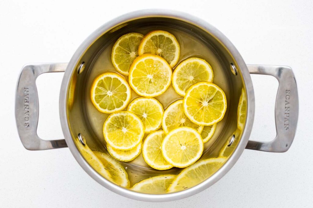 Sliced lemons with lemon juice and salt in a stainless steel pot viewed from above.