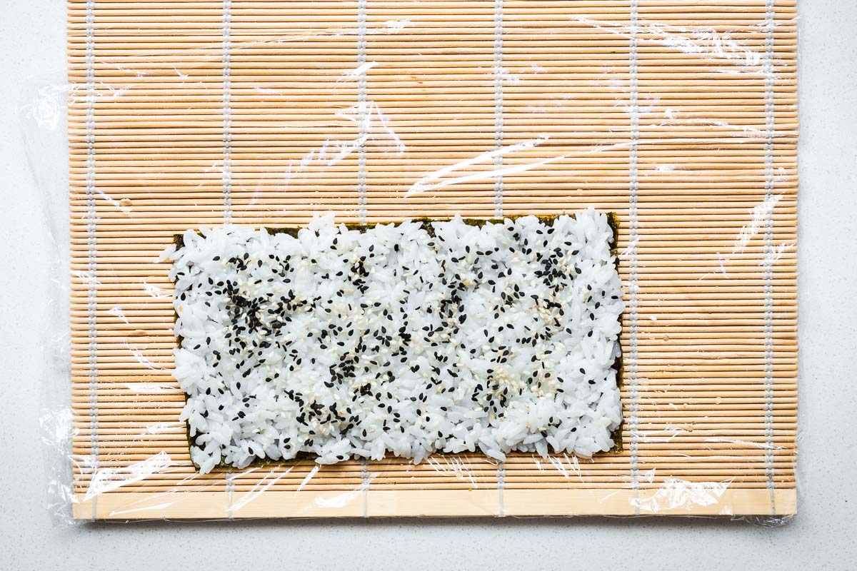 A piece of nori seaweed topped with sushi rice sprinkled with sesame seeds viewed from above.