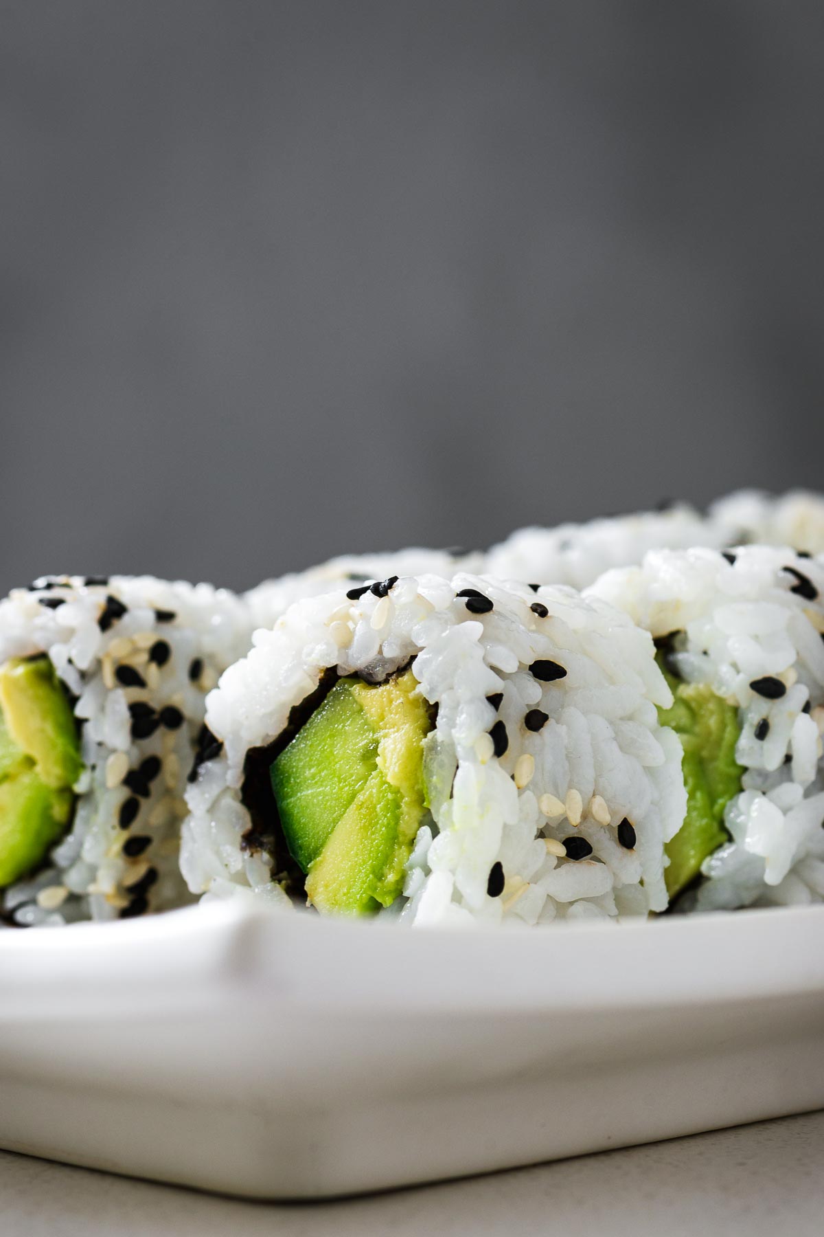 A close-up view of an uramaki sushi roll filled with avocado and cucumber, sprinkled with sesame seeds.