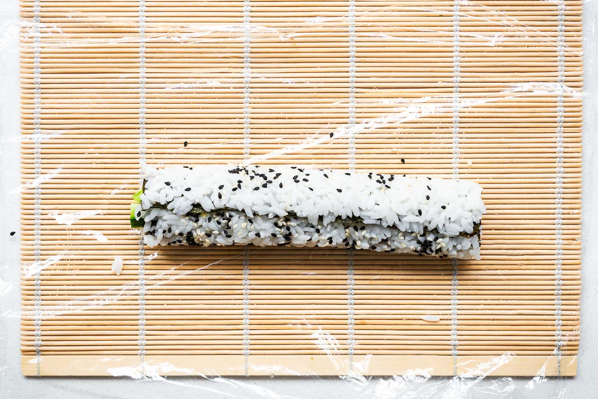 A whole uramaki sushi roll (inside-out roll) on a sushi mat before if it sliced.