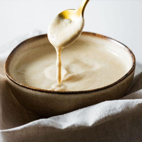 A close-up of a creamy lemon tahini sauce in a ceramic bowl with a golden spoon.