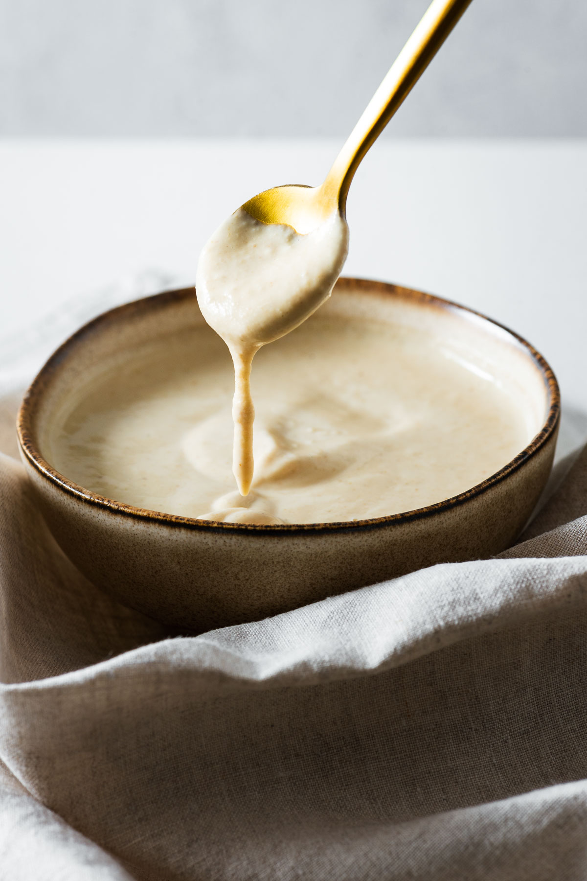 A close-up of a creamy lemon tahini sauce in a ceramic bowl with a golden spoon.
