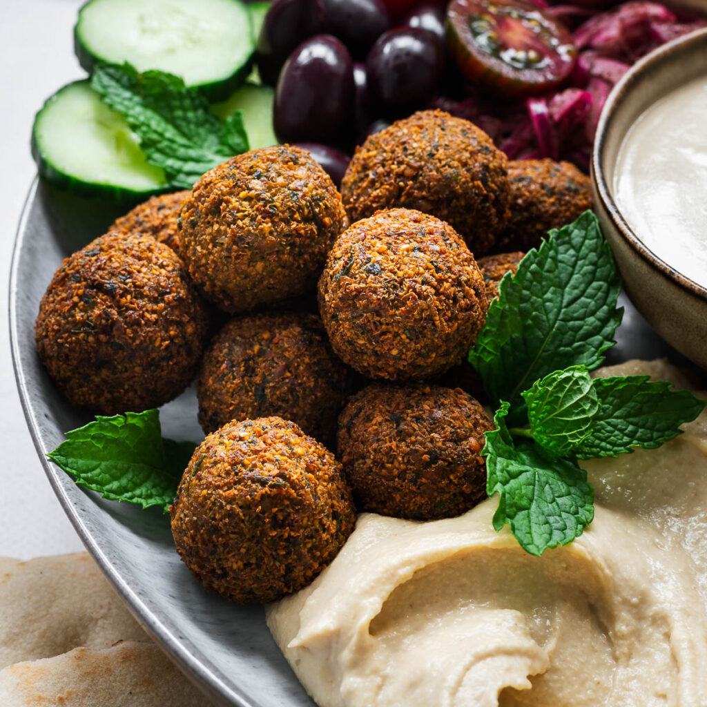 Golden brown Middle Eastern falafel on a plate with tahini sauce, hummus and fresh salad.
