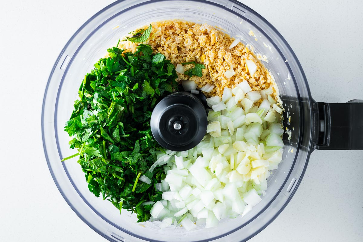 Herb falafel ingredients in the bowl of a food processor.