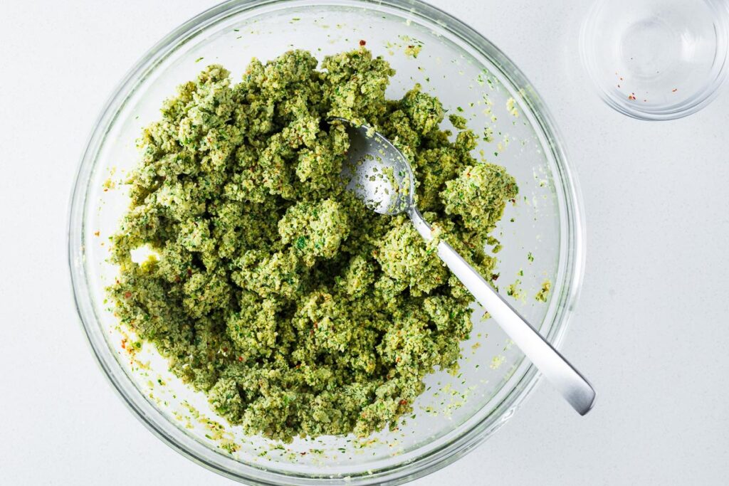Green falafel mixture of soaked dried chickpeas and fresh herbs in a large mixing bowl.