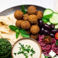 A falafel plate with crispy falafel balls, tahini falafel sauce, sumac onions, humus, zhoug and fresh vegetables.