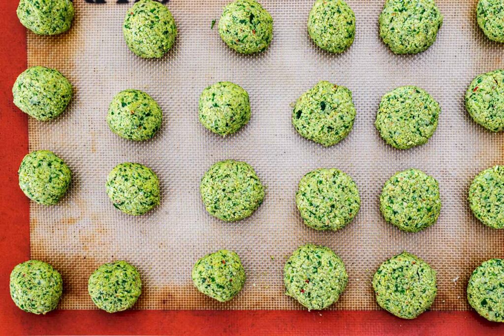 Green herbed falafel mixture shaped into balls and small patties on a silicone baking mat.