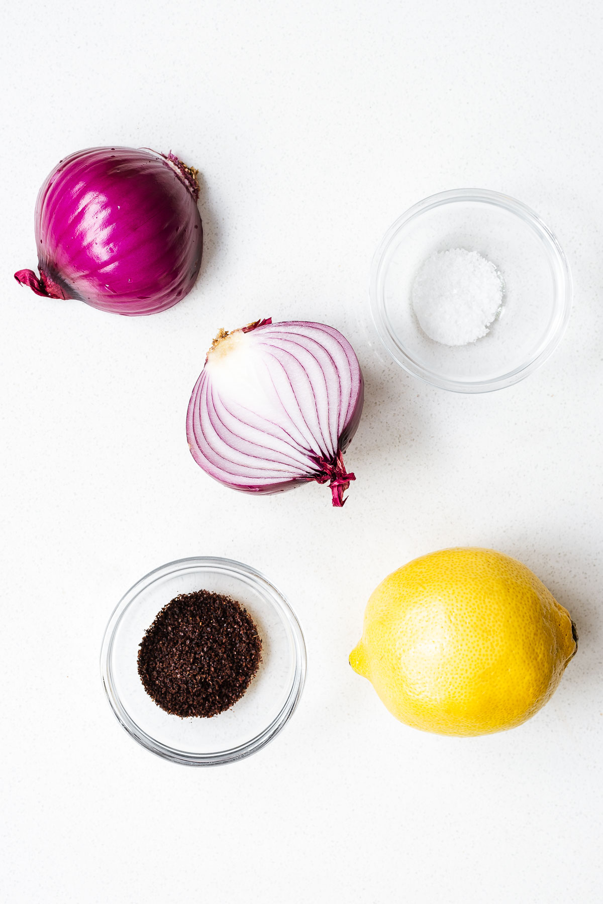 The ingredients for sumac onions including a red onions, lemon juice, sumac powder and salt.